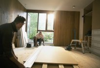 Trabajadores de la construcción midiendo tablero de madera en casa - foto de stock