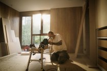 Travailleur de la construction utilisant une scie électrique pour couper le bois dans la maison — Photo de stock