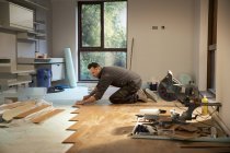 Trabalhador da construção civil que estabelece piso de madeira em casa — Fotografia de Stock