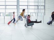 Verspieltes Paar schiebt Gepäckwagen in Flughafen — Stockfoto