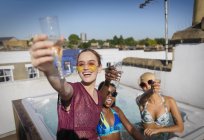 Портрет впевнені, безтурботні молоді жінки друзі п'ють шампанське в сонячній гарячій ванні на даху — стокове фото