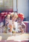Tonto, juguetón jóvenes amigas tomando selfie con cámara de teléfono en la cafetería - foto de stock