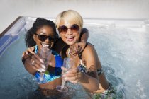 Portrait exubérantes jeunes femmes amies buvant du champagne dans un bain à remous ensoleillé — Photo de stock