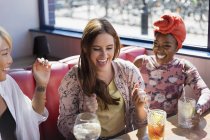 Mujeres jóvenes felices y emocionadas tomando cócteles en el restaurante - foto de stock
