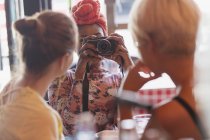 Mujer joven fotografiando amigos con cámara en restaurante - foto de stock