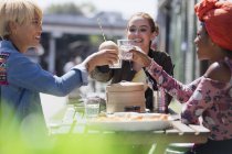Giovani donne amiche brindare bicchieri d'acqua a fioco pranzo sum al caffè marciapiede soleggiato — Foto stock