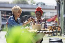Щасливі молоді жінки друзі насолоджуються сніданком у сонячному тротуарному кафе — стокове фото