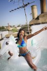 Ritratto giocoso, spensierata giovane donna in bikini su pegaso gonfiabile nella vasca idromassaggio soleggiata sul tetto — Foto stock
