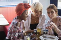 Young women friends using smart phone at restaurant table — Stock Photo