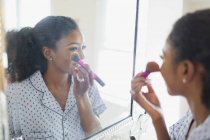 Young woman getting ready, applying makeup in bathroom mirror — Stock Photo