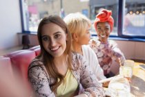 Retrato sonriente mujer joven en restaurante soleado con amigos - foto de stock