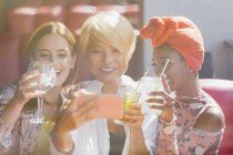 Young women friends drinking cocktails and taking selfie with smart phone in sunny bar — Stock Photo
