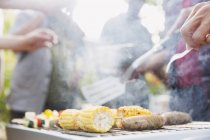 Corncobs, sausages and vegetable skewers cooking on barbecue grill — Stock Photo