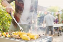 Человек жарит кукурузу, колбасу и овощные кебабы — стоковое фото
