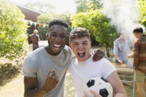 Portrait enthusiastic young men with soccer ball cheering, enjoying back yard barbecue — Stock Photo