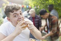 Portrait hungry teenage boy eating hamburger at backyard barbecue — Stock Photo