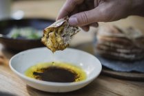 Chiudi a mano immergendo il pane nell'olio d'oliva e nell'aceto balsamico — Foto stock