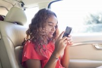 Tween chica usando teléfono inteligente en asiento trasero del coche - foto de stock
