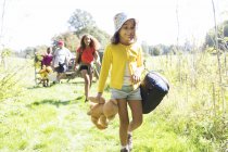 Girl camping with family, carrying sleeping bag and teddy bear — Stock Photo