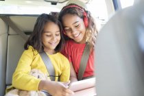 Sisters using digital tablet in back set of car — Stock Photo