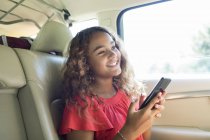 Посміхається дівчина створити проміжні кадри, використовуючи смарт-телефону в задньому сидінні автомобіля — стокове фото