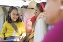 Sorelle felici che cavalcano sul sedile posteriore dell'auto con tablet digitale — Foto stock