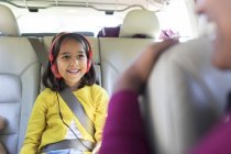 Chica sonriente con auriculares montando en el asiento trasero del coche - foto de stock