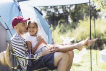 Happy, affectionate father holding daughter in lap at sunny campsite — Stock Photo