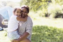 Portrait affectionate mother holding daughter at sunny campsite — Stock Photo