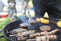 Man barbecuing hamburgers, kebabs and corn cobs — Stock Photo