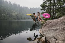 Jeune couple ludique avec anneaux gonflables sautant dans un lac isolé, Squamish, Colombie-Britannique, Canada — Photo de stock
