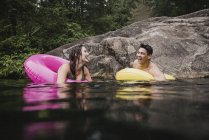 Feliz pareja joven flotando en anillos inflables en el lago - foto de stock