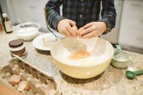 Chico horneando, agrietando huevo en un tazón en la cocina - foto de stock