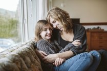 Ласковые мать и дочь обнимаются на диване в гостиной — стоковое фото