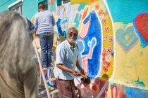 Старший чоловік волонтер малює яскраві фрески на сонячній стіні — стокове фото