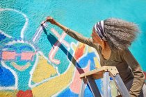 Старша жінка малює яскраві фрески на сонячній стіні — стокове фото