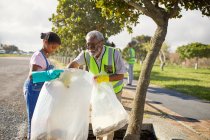 Grandfather and granddaughter volunteers cleaning up litter in sunny park — Stock Photo