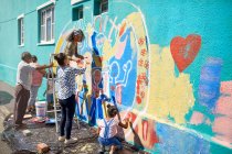 Community volunteers painting multicolor mural on sunny urban wall — Stock Photo