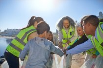 Volunteers forming huddle, cleaning up litter on sunny beach — Stock Photo