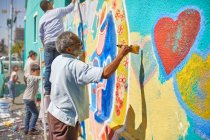 Старший чоловік малює фрески на сонячній міській стіні — стокове фото