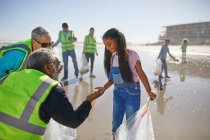 Freiwillige Großeltern und Enkelinnen räumen Müll am sonnigen, nassen Sandstrand auf — Stockfoto