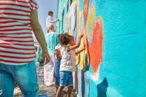 Menina voluntária pintura mural vibrante na parede ensolarada — Fotografia de Stock