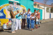 Heureux bénévoles communautaires célébrant murale peinte sur un mur urbain ensoleillé — Photo de stock