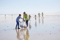 Madre e figlio volontari pulizia della lettiera sulla spiaggia di sabbia soleggiata e bagnata — Foto stock