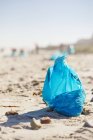 Saco de lixo de limpeza azul na praia ensolarada e arenosa — Fotografia de Stock