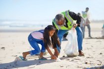Voluntários do avô e da neta limpando ninhada na praia ensolarada e arenosa — Fotografia de Stock