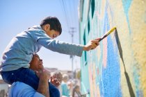 Father and son volunteers painting mural on sunny wall — Stock Photo