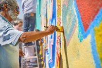 Старший чоловік малює фрески на сонячній стіні — стокове фото