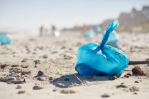 Blue bag of litter on sunny, sandy beach — Stock Photo