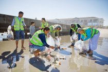 Des bénévoles nettoient la litière sur une plage de sable humide et ensoleillée — Photo de stock